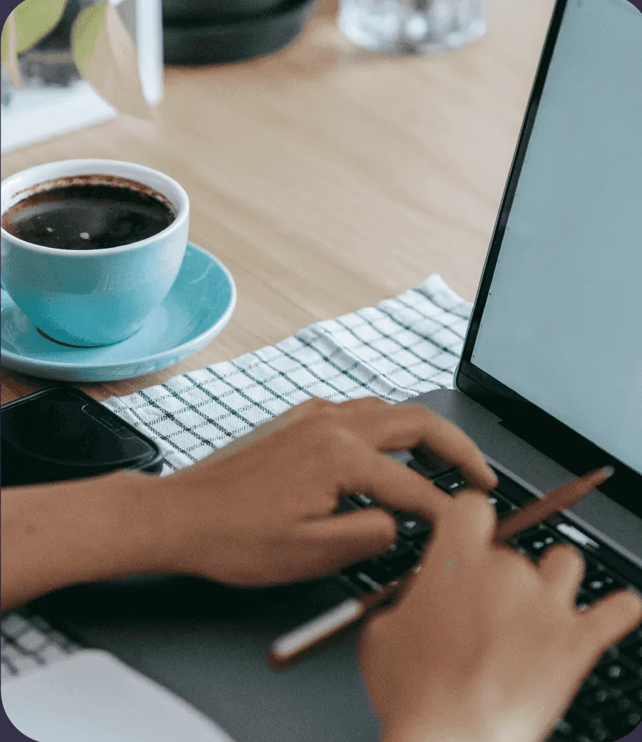 Mãos digitando num laptop ao lado de uma xícara de café